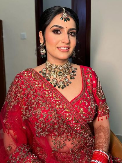 This regal bridal look is all about timeless grace. The makeup features a classic smokey eye and a perfectly sculpted base to complement the rich red outfit and heavy jewelry.