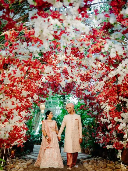 A romantic portrait of the couple framed by a stunning red and white floral arch. The way they look at each other captures the magic of the moment.