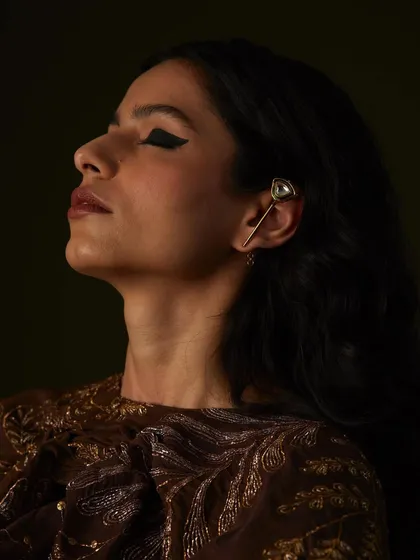 A close-up on the model's face, showcasing the dramatic cat-eye makeup and a delicate ear cuff.