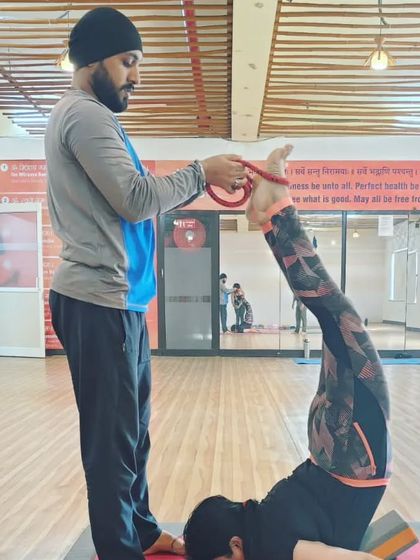 Assisting a student with a strap in a variation of Sarvangasana (Shoulder Stand). Props help to achieve the correct alignment and hold the pose safely.