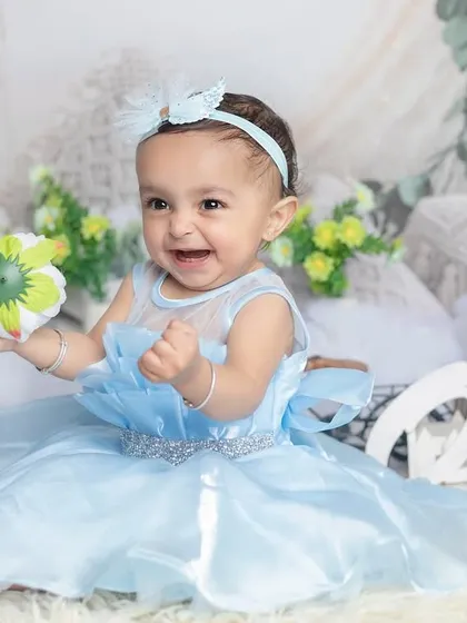 A bright, joyful smile from the birthday girl. The light blue dress and floral background create a fresh, happy atmosphere.
