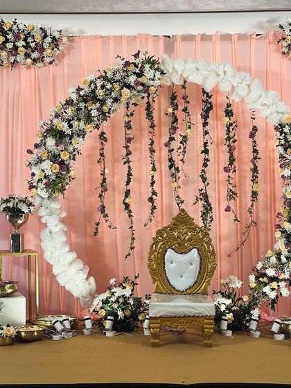 The combination of peach drapes and a multi-colored floral arch creates a soft yet festive look, perfect for daytime celebrations like a half-saree ceremony.