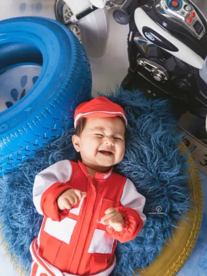 A few action shots from an F1 and racing-inspired photoshoot. The baby is styled in a red racing uniform, captured with fun expressions among tires and toy vehicles.