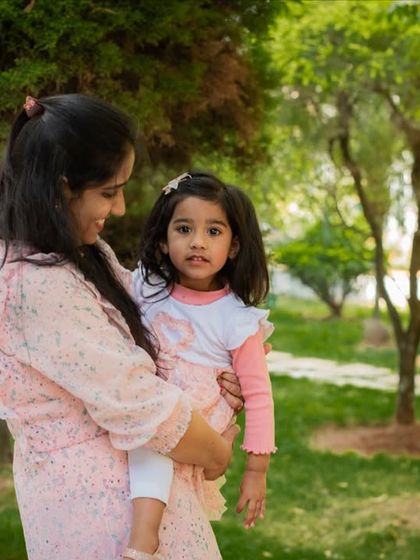 A mother holds her daughter in a beautiful green park. The soft light and their gentle interaction make for a sweet and timeless mommy-and-me photo.