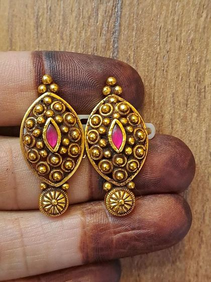 A pair of oval-shaped antique gold-plated earrings with a central pink stone. The design is elegant and has a beautiful vintage charm.