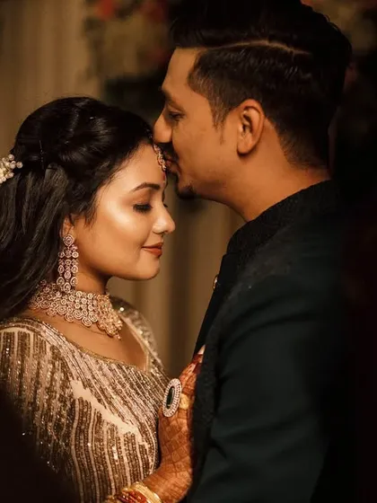 A tender moment between the couple during their Sangeet night. The groom places a gentle kiss on his bride's forehead, a quiet moment of affection amidst the grand celebration.