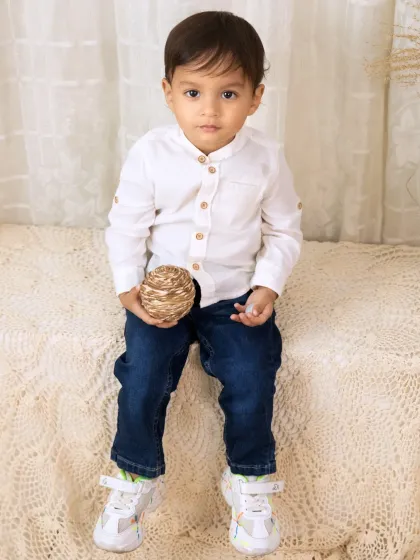 A charming solo portrait of a little boy in a smart white shirt and jeans, posing confidently in our boho studio.