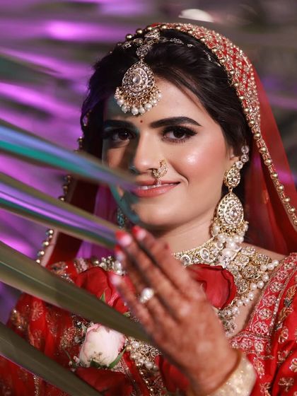 A creative shot of the bride peeking through palm leaves. Her makeup is flawless, with a perfectly winged liner and a radiant smile that shines through.