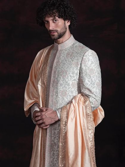 This angle shows the beautiful drape and texture of the all-over embroidered sherwani. The silk stole adds a layer of softness and tradition, balancing the structured fit of the garment. It is a timeless piece for a classic wedding ceremony.