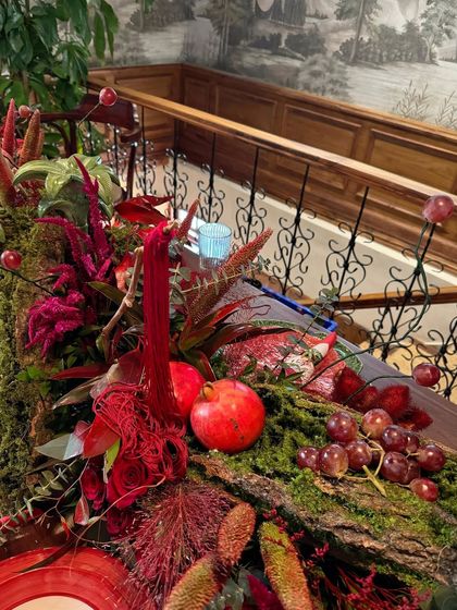 A detail shot of our rustic and opulent table runner. A moss-covered log is adorned with rich red florals, pomegranates, and grapes, creating a tablescape that feels like a decadent, old-world feast.