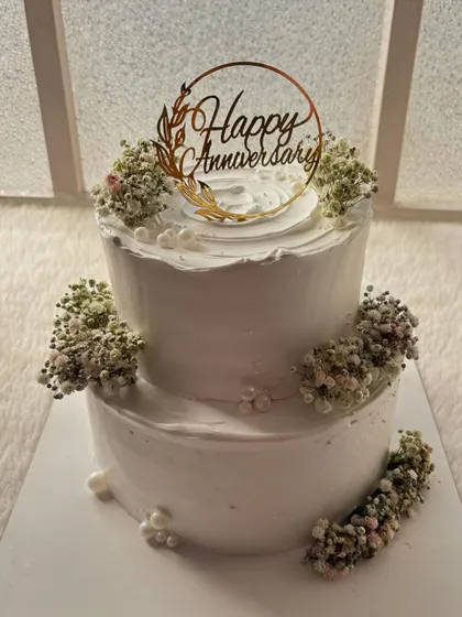 Another angle of the minimalist two-tier anniversary cake. The "Happy Anniversary" topper adds a touch of gold to the pure white design.
