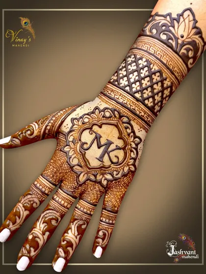 A stylish monogram design for a guest or family member. The initials 'MK' are placed inside an ornate crest on the back of the hand, surrounded by traditional patterns.