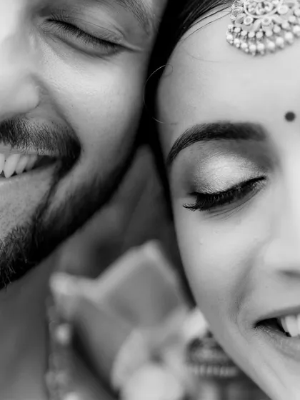 A tight close-up in black and white, capturing the joyful smiles and closed eyes of the couple. This image is pure emotion, highlighting details like the bride's maang tikka.