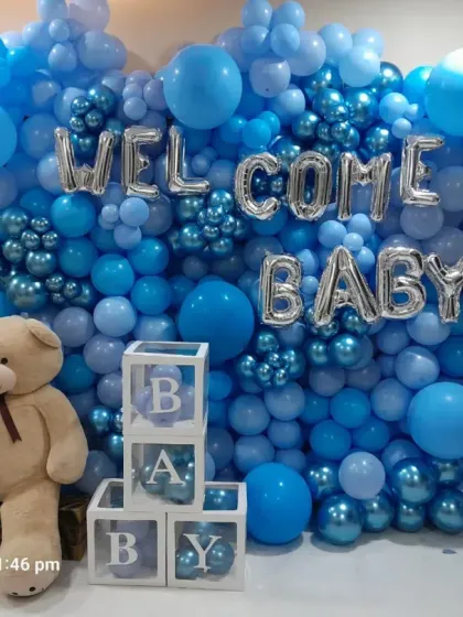 A full balloon wall in shades of blue makes a big impact for a welcome home celebration. The silver 'WELCOME BABY' foil balloons, a large teddy bear, and transparent 'BABY' blocks complete this grand gesture.