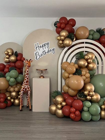 A modern and chic safari-themed setup using muted, earthy tones. The decoration features elegant arched backdrops and organic balloon arrangements in green, brown, and gold.