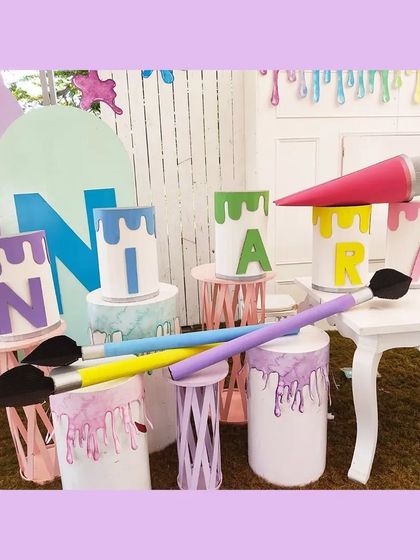 For an art-themed party, I designed this vibrant installation featuring oversized paint cans spelling out the birthday girl's name, 'NIARA'. The giant paintbrushes and dripping paint effect added a playful, creative touch to the decor.