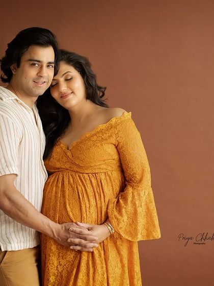 A warm and earthy studio portrait. The brown backdrop and the couple's relaxed pose create a feeling of comfort, intimacy, and grounded love.