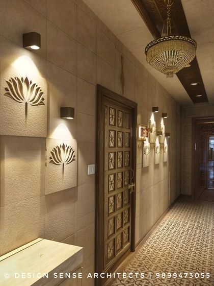 An elegant hallway featuring custom sandstone panels with a lotus motif, spotlit for dramatic effect. The traditional floor tiles and ornate door complete this Indian-inspired design.