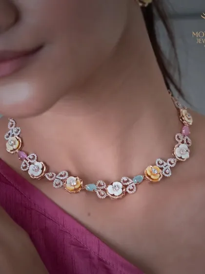 A beautiful floral necklace with mother-of-pearl flowers, colourful gemstones, and diamond-studded leaves, worn by a model.