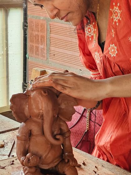 A student works on her Ganesha idol, with another piece visible in the background. The studio is a busy, creative space during these workshops.