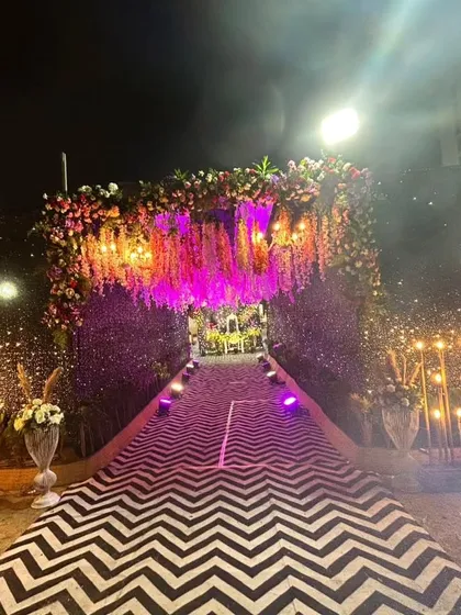 A breathtaking entrance for a grand celebration, featuring a walkway covered in a chevron pattern, lined with sparkling lights, and a lush floral archway overhead.