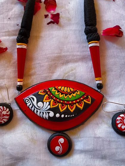 A duplicate image of the red, black, and white eye-shaped pendant with a different alpona motif.