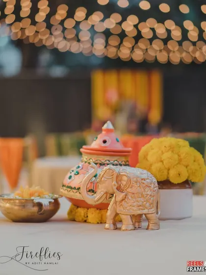 A table centerpiece featuring a hand-painted pot, a brass elephant, and a bowl of marigolds, combining several traditional Indian decor elements.
