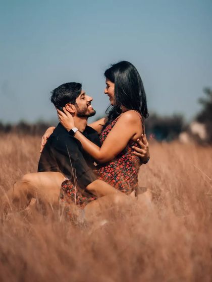 A romantic gaze shared between a couple sitting in a field of golden grass. The warm, soft light enhances the intimate and loving atmosphere of the portrait.