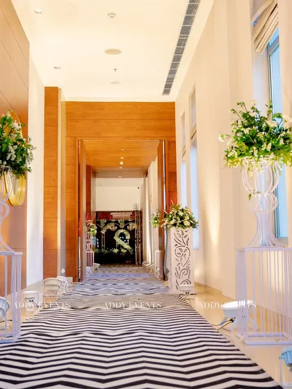 A long corridor transformed with a bold chevron-patterned carpet and lined with elegant floral arrangements on pedestals. This shows how we use flooring and decor to guide guests and build anticipation.
