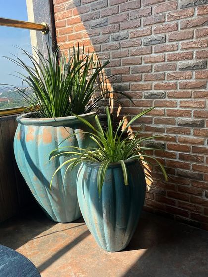 A pair of rustic teal planters adding a pop of colour against a brick wall. The weathered finish gives them a unique, vintage charm.