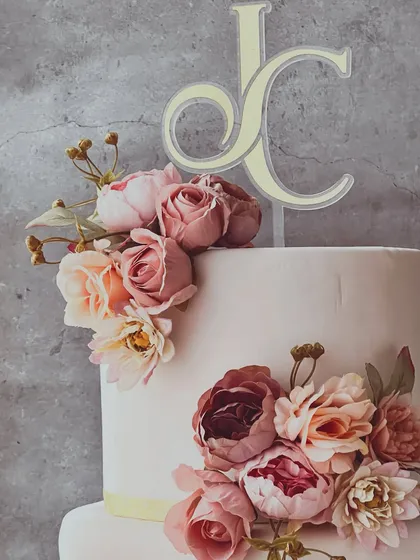 A close-up detail shot of the wedding cake, focusing on the intricate sugar flowers and the elegant custom "JC" monogram topper.