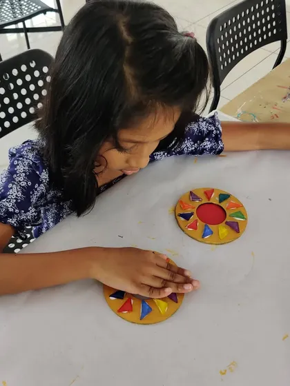 A child carefully places colorful mosaic tiles onto a circular base to create a beautiful T-light holder for Diwali.