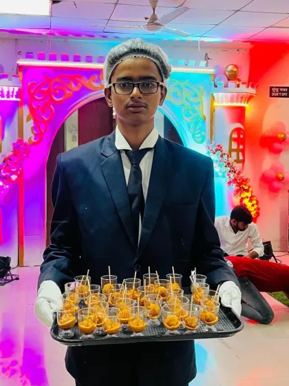 A waiter in full uniform serving starters in shot glasses at a birthday party. This kind of presentation adds a modern touch to the service.
