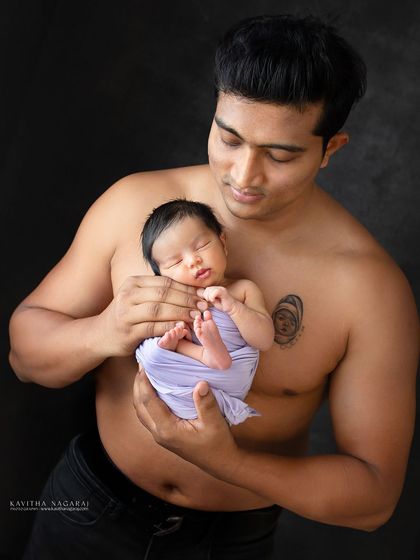A father holds his newborn daughter, her tiny body wrapped in purple, resting against his chest. A beautiful portrait of safety and love.