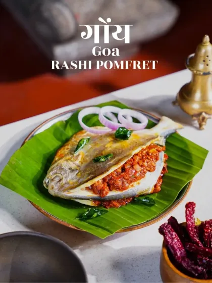 Goan Rashi Pomfret, stuffed with fiery red masala and served on a banana leaf. The clean, bright styling highlights the textures and colors of this iconic coastal dish.