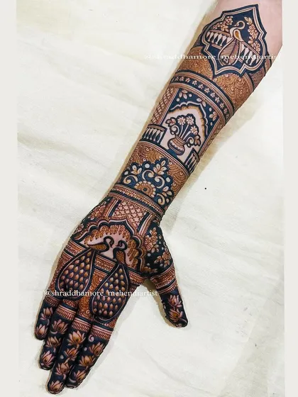 A close-up of a bridal arm featuring majestic peacocks on the palm and a traditional kalash on the forearm, all framed by beautiful arches.