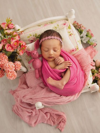 A classic and sweet setup featuring a baby girl sleeping on a tiny bed, accompanied by a knitted bunny toy and beautiful pink flowers.