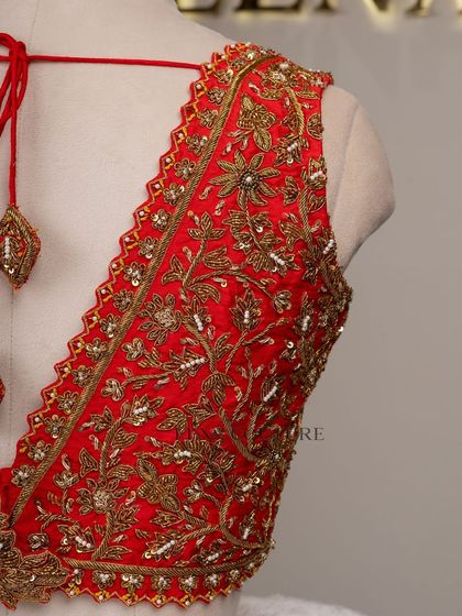This sleeveless red blouse is perfect for a bold bridal statement. It features a deep V-neckline and is heavily embellished with intricate gold floral zardozi work, creating a rich and luxurious feel.