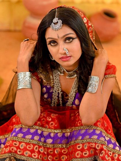 A seated portrait on the Rajasthani set, where the model's pose conveys a sense of waiting and contemplation. The composition uses the props to frame the subject effectively.