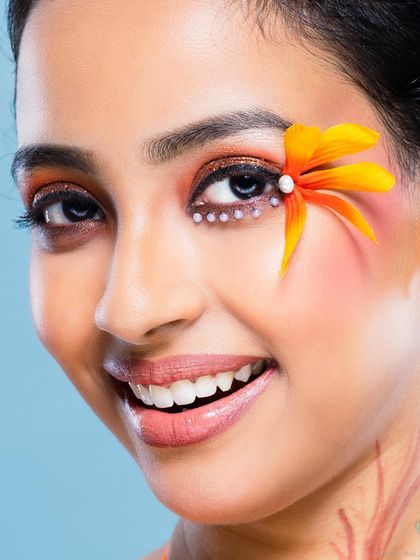 A bright and happy beauty portrait with creative floral makeup. The model's wide smile and the cheerful orange tones create a joyful, vibrant image.