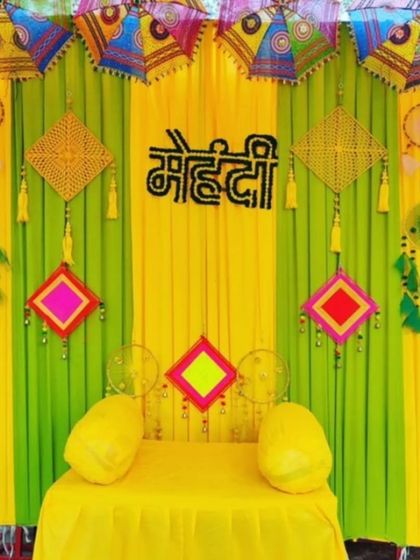 A very colorful and traditional Mehandi seating with bright yellow and green drapes. The backdrop is decorated with Rajasthani umbrellas and vibrant hangings for a festive look.