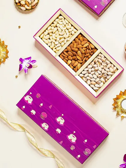 A chic and modern flatlay of a purple dry fruit gift box. The clean composition with orchids and diyas gives a contemporary yet festive feel, appealing to a modern aesthetic.