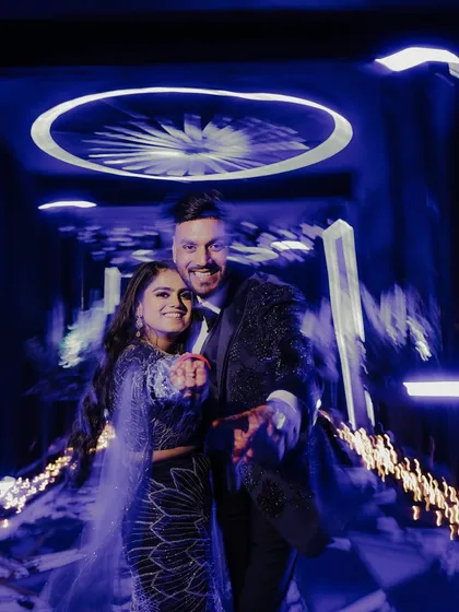 A fun and energetic candid shot of the couple. They point towards the camera with big smiles, captured with a creative motion blur effect that conveys the fast-paced excitement of the party.