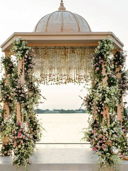 A close up of the picturesque varmala mandap we built by the serene backwaters. The pillars are wrapped in spiraling arrangements of pastel roses and fresh greenery, blending seamlessly with the garden environment.