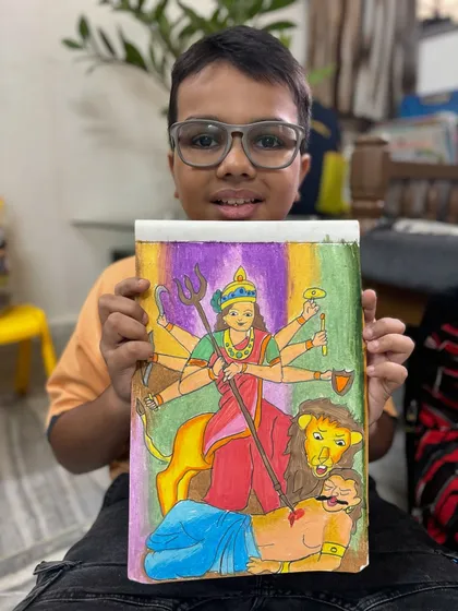 A 5th-grade student proudly displays his powerful drawing of Goddess Durga. We explore divine feminine energy and mythology through our artistic creations.