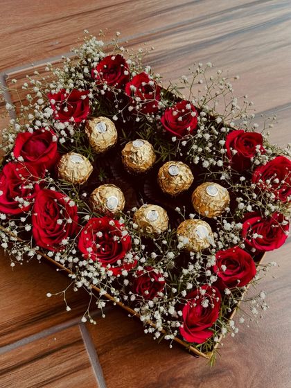 A luxurious square box arrangement featuring rich red roses, delicate baby's breath, and a centerpiece of golden Ferrero Rocher chocolates. It's a perfect blend of classic romance and sweet indulgence.