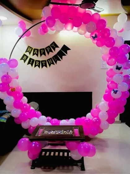 A simple and sweet circular balloon arch in pink and white for a birthday. The 'Happy Birthday' banner and butterfly accents add a charming touch to this home setup.