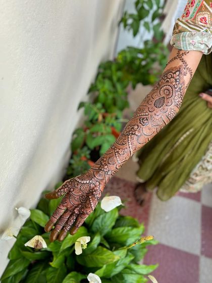 A single-arm shot against a natural green background, which makes the henna color look so rich.