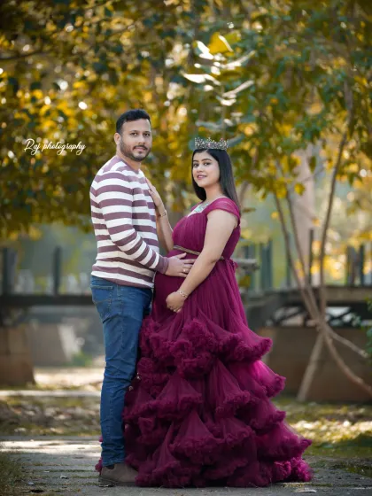 A classic couple's portrait in a park setting. The mother-to-be looks radiant in a wine-colored ruffled gown and crown.