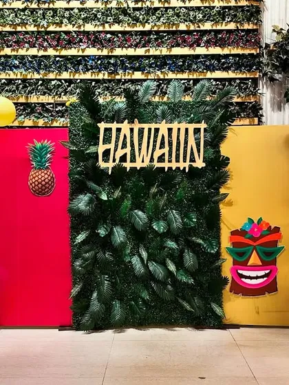 Aloha! A vibrant and colorful Hawaiian-themed party backdrop. We used bright balloon garlands, fun props like a tiki mask and pineapple, and a leafy green wall to bring the tropical vibes.